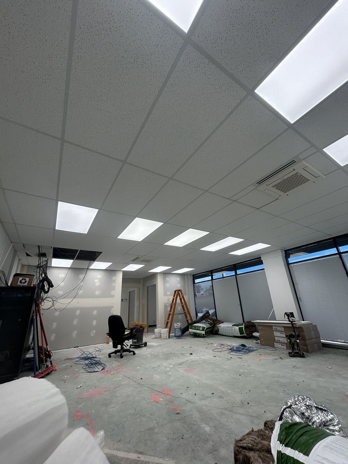 Suspended tile ceiling in a commercial office fitout with lighting panels and an air conditioning cassette